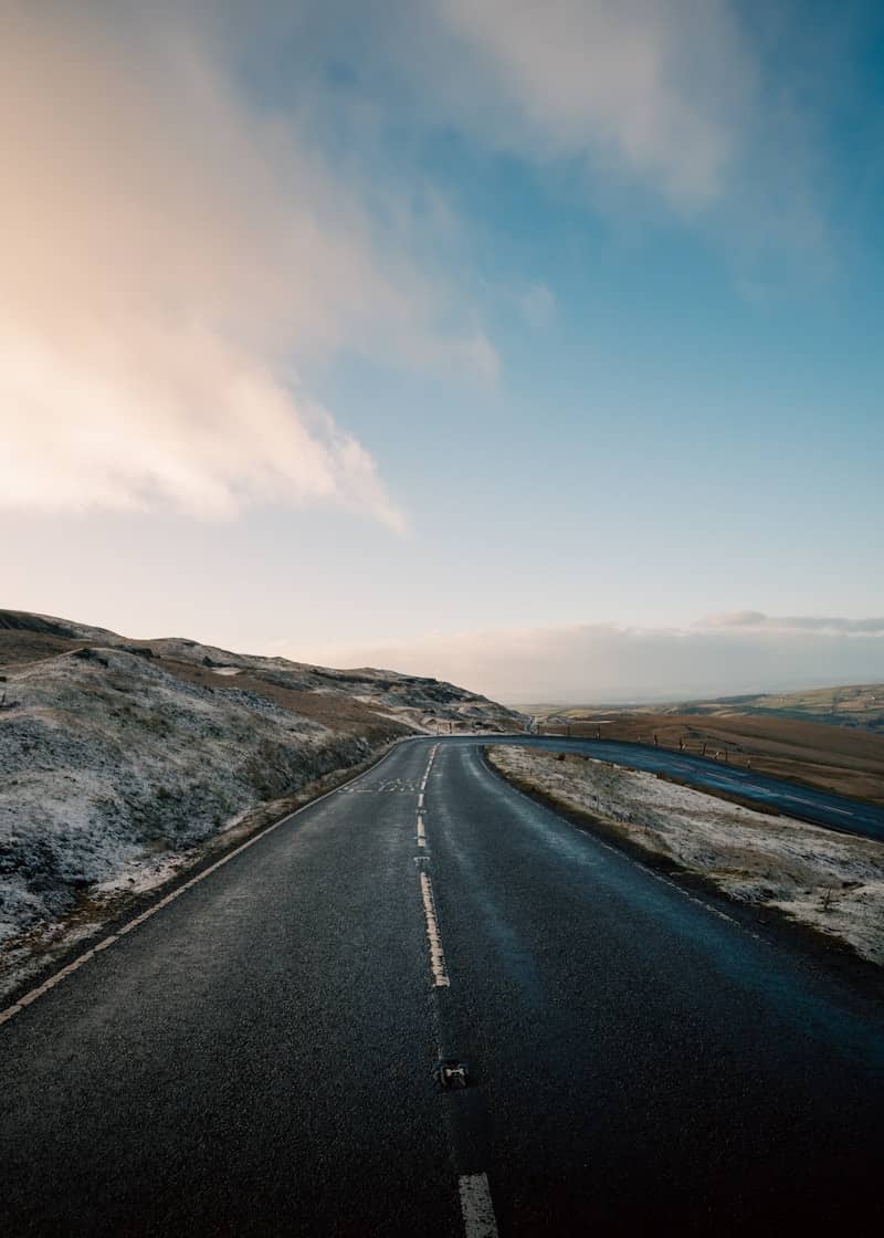 Empty asphalt road through rolling hills under sky