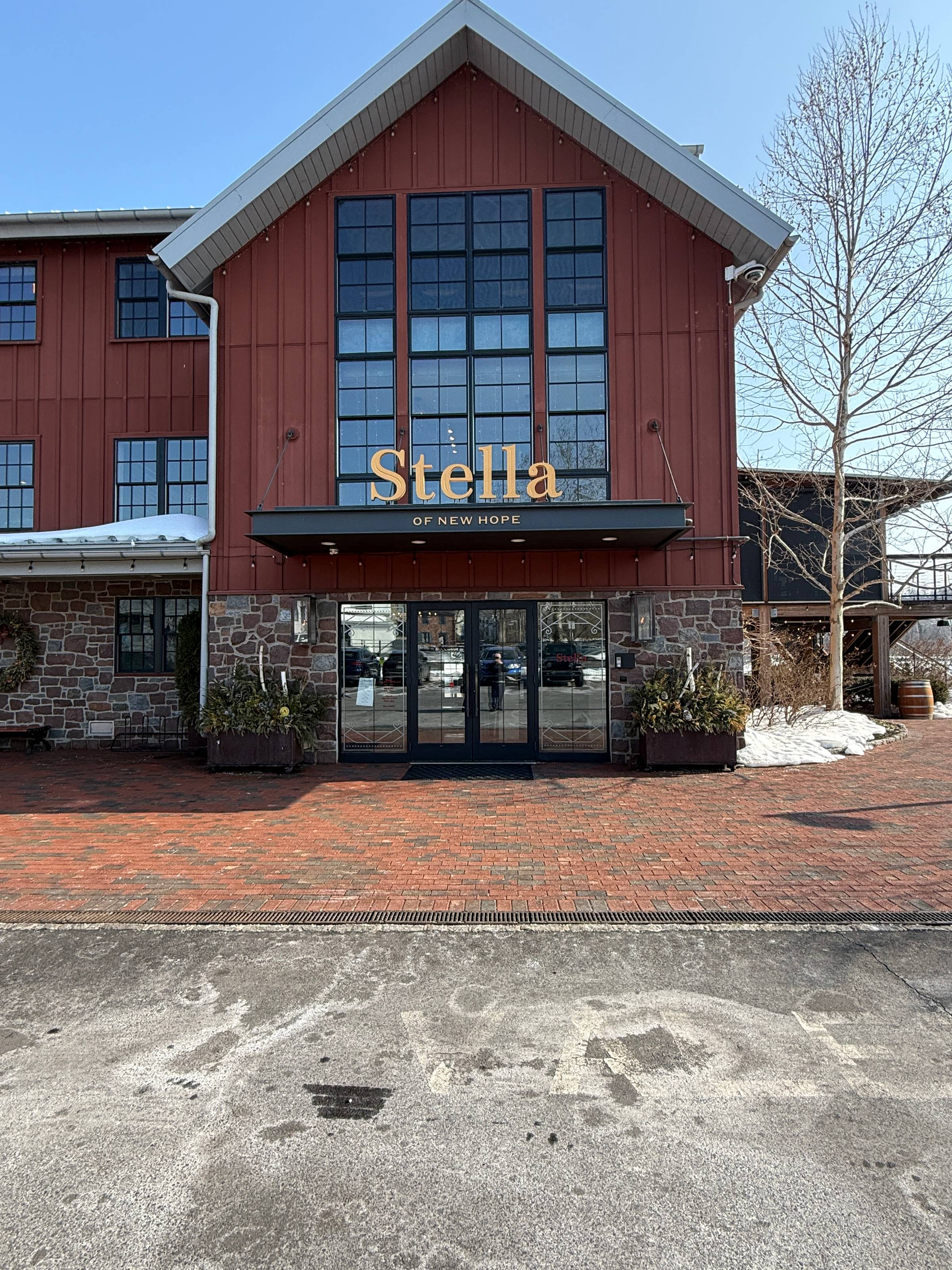 Exterior of Stella restaurant in New Hope featuring a red facade, tall grid windows, stone base, and brick walkway leading to the entrance.