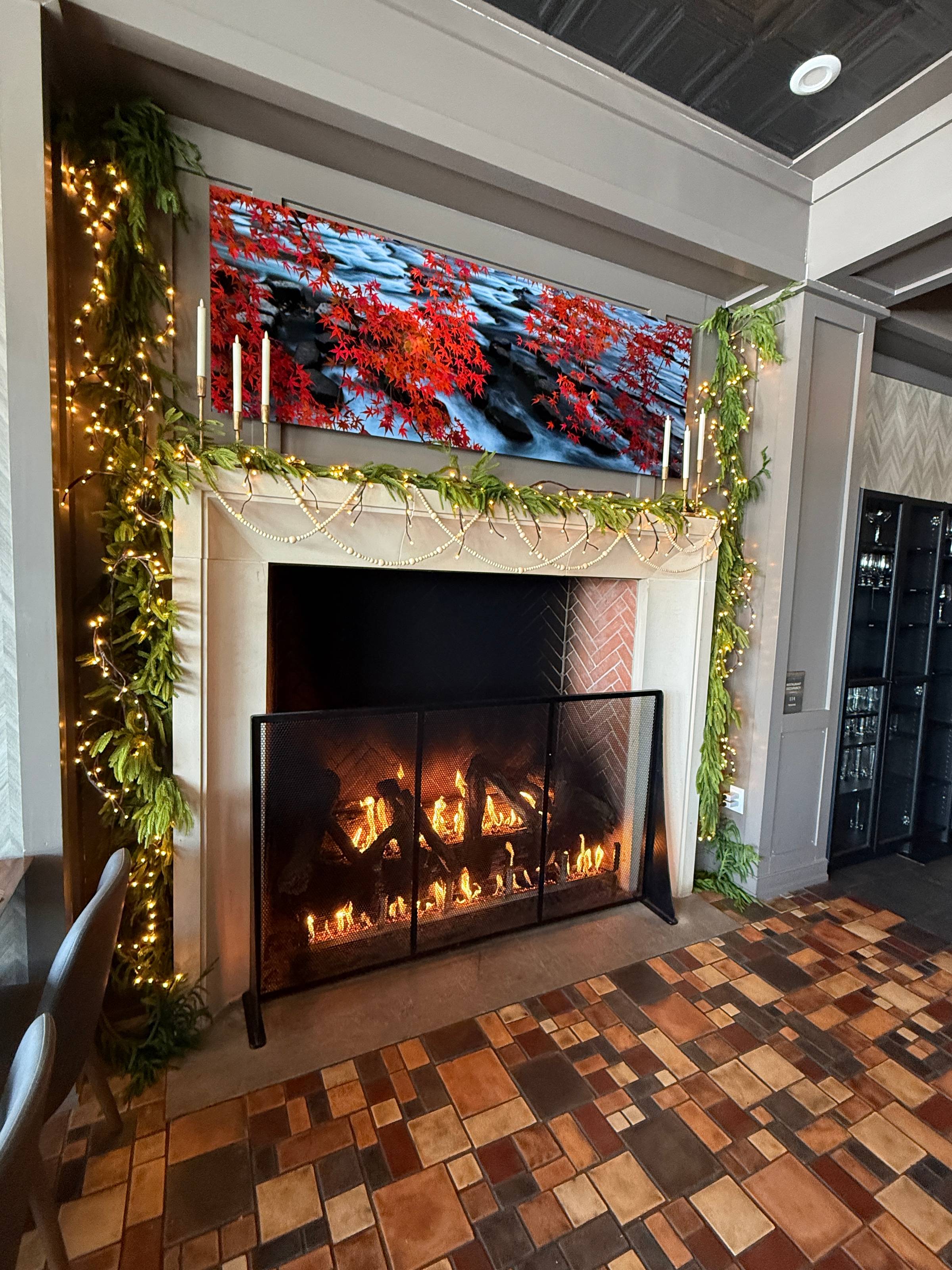 Cozy fireplace with burning fire, mantel decorated with greenery and warm string lights at Stella restaurant.