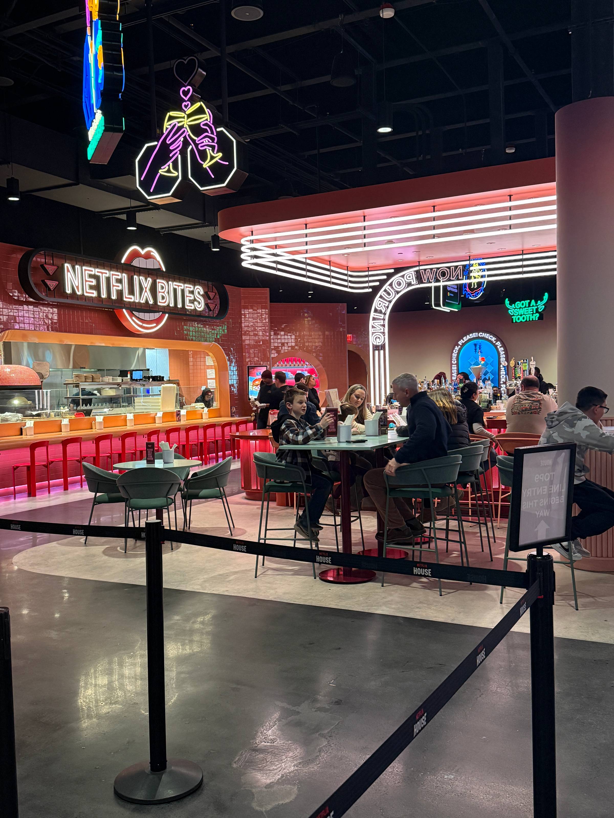 Interior of Netflix Bites eatery at Netflix House, featuring neon signs, a bright red counter, and guests seated at tables.