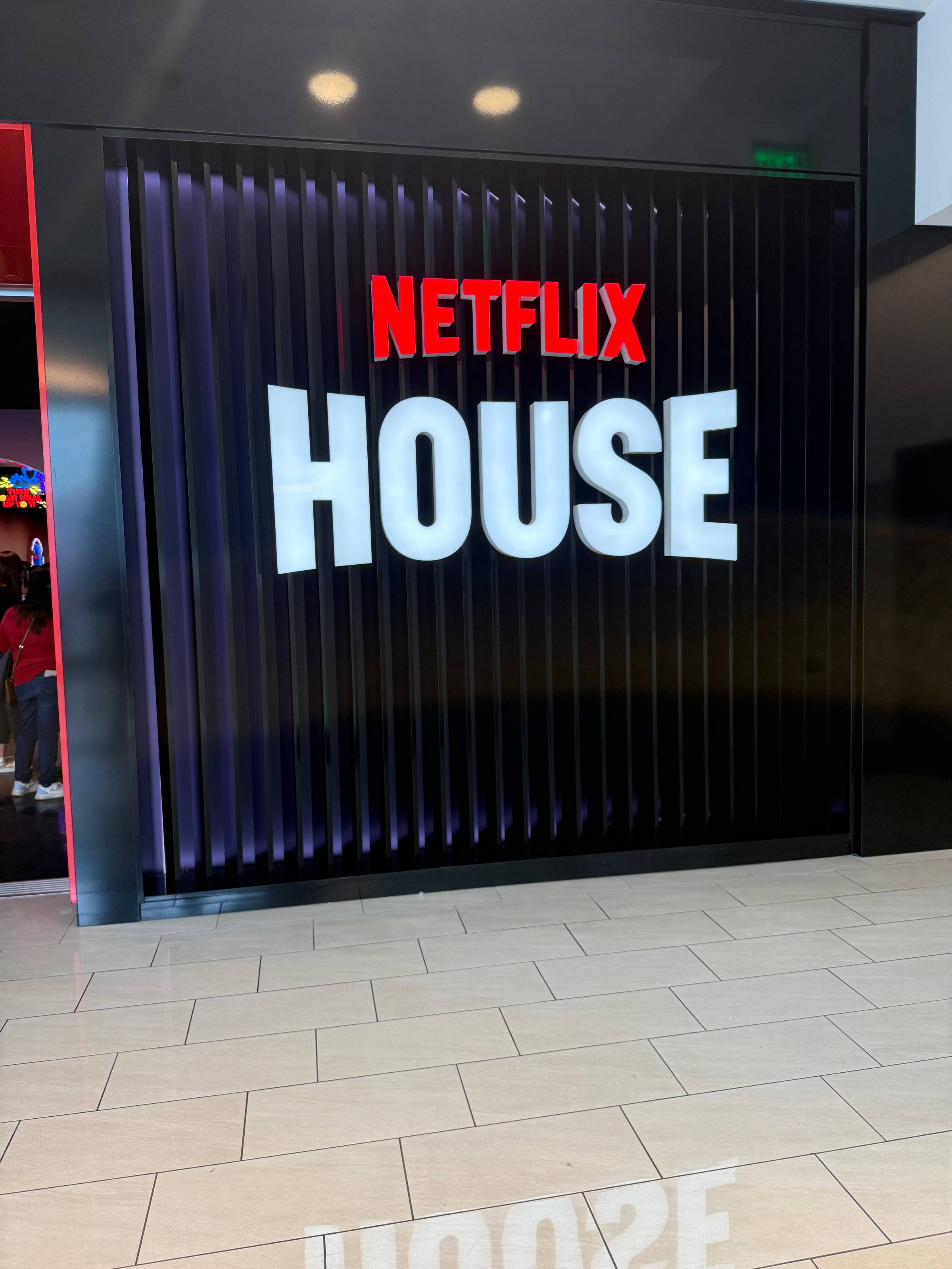 Large illuminated Netflix House sign with red and white lettering mounted on a dark, vertically paneled wall inside the venue.