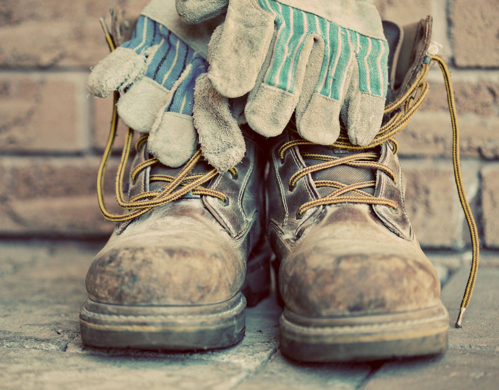 Worn work boots and leather gloves on a farm, representing steady daily work over time