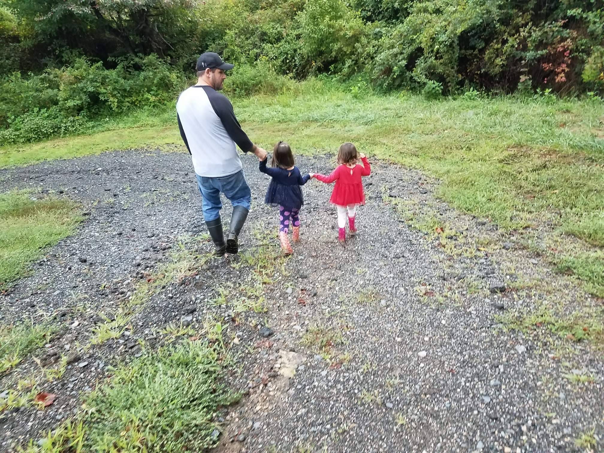 Farmer walking hand-in-hand with his two young daughters on the farm