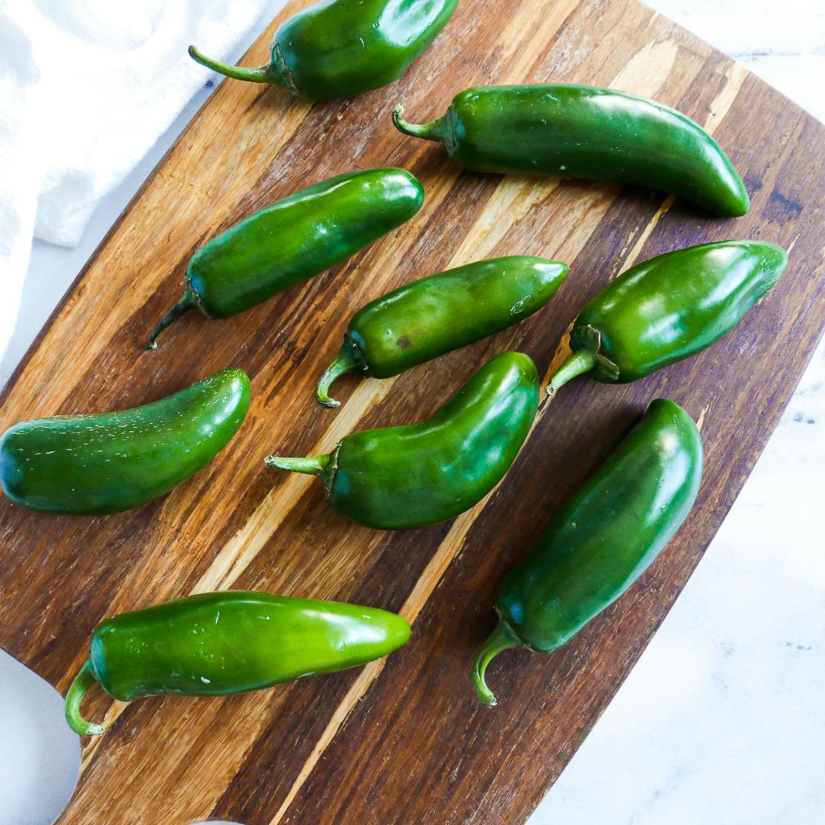 Several jalapeño peppers arranged on a wooden cutting board.