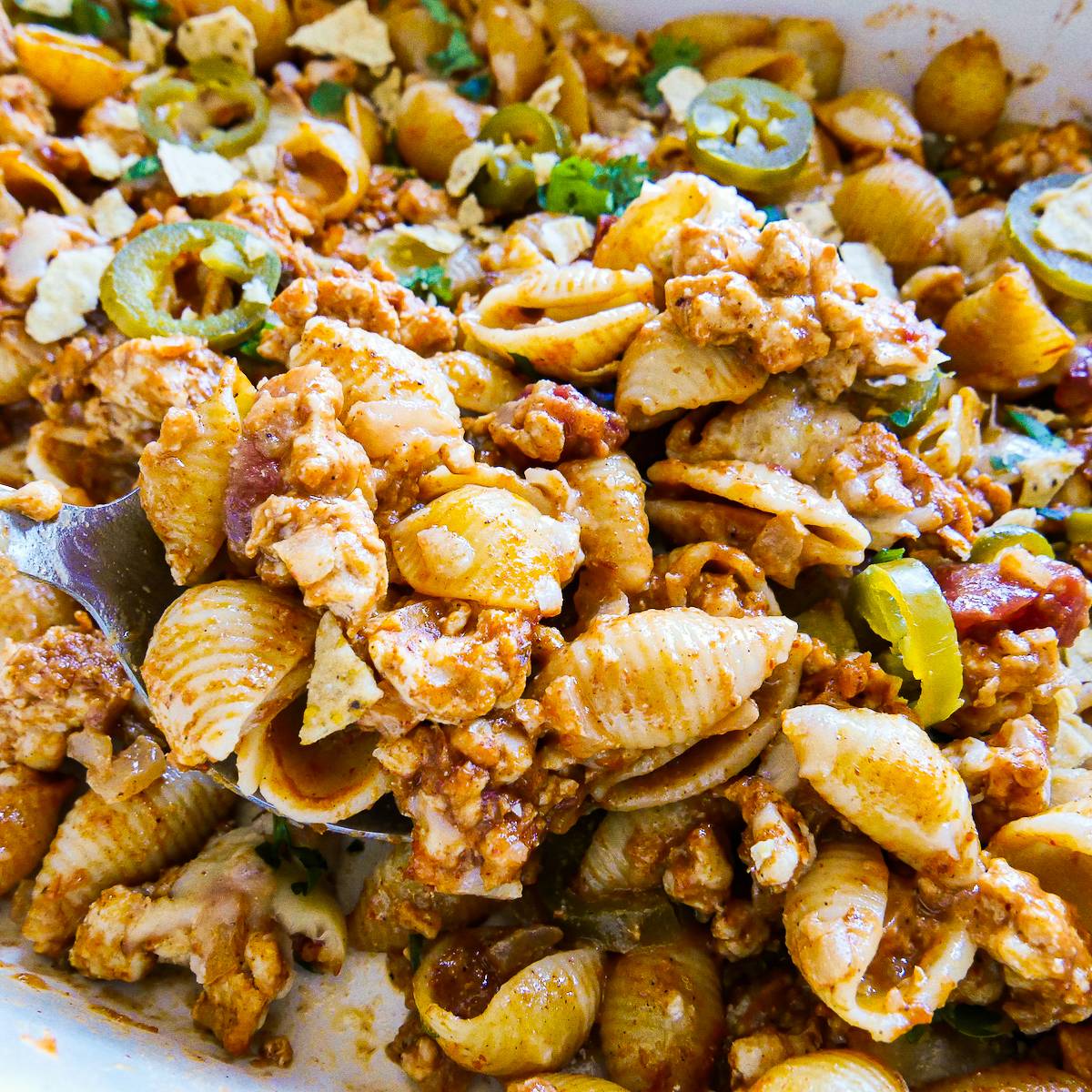 Spooning up taco pasta casserole from a baking dish.