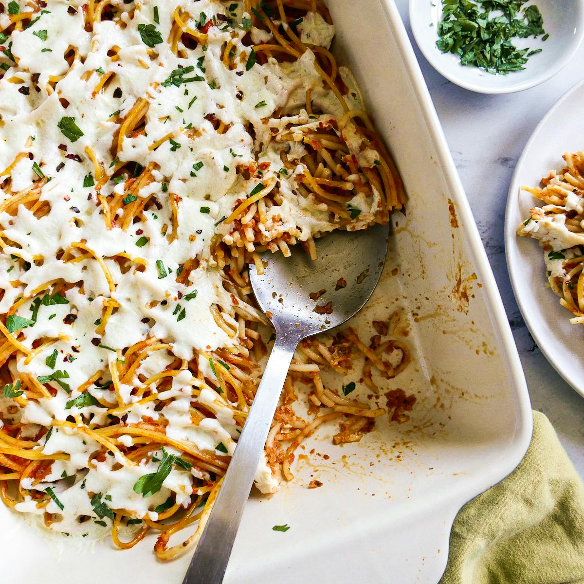Spaghetti casserole with a large spoon and a green napkin.