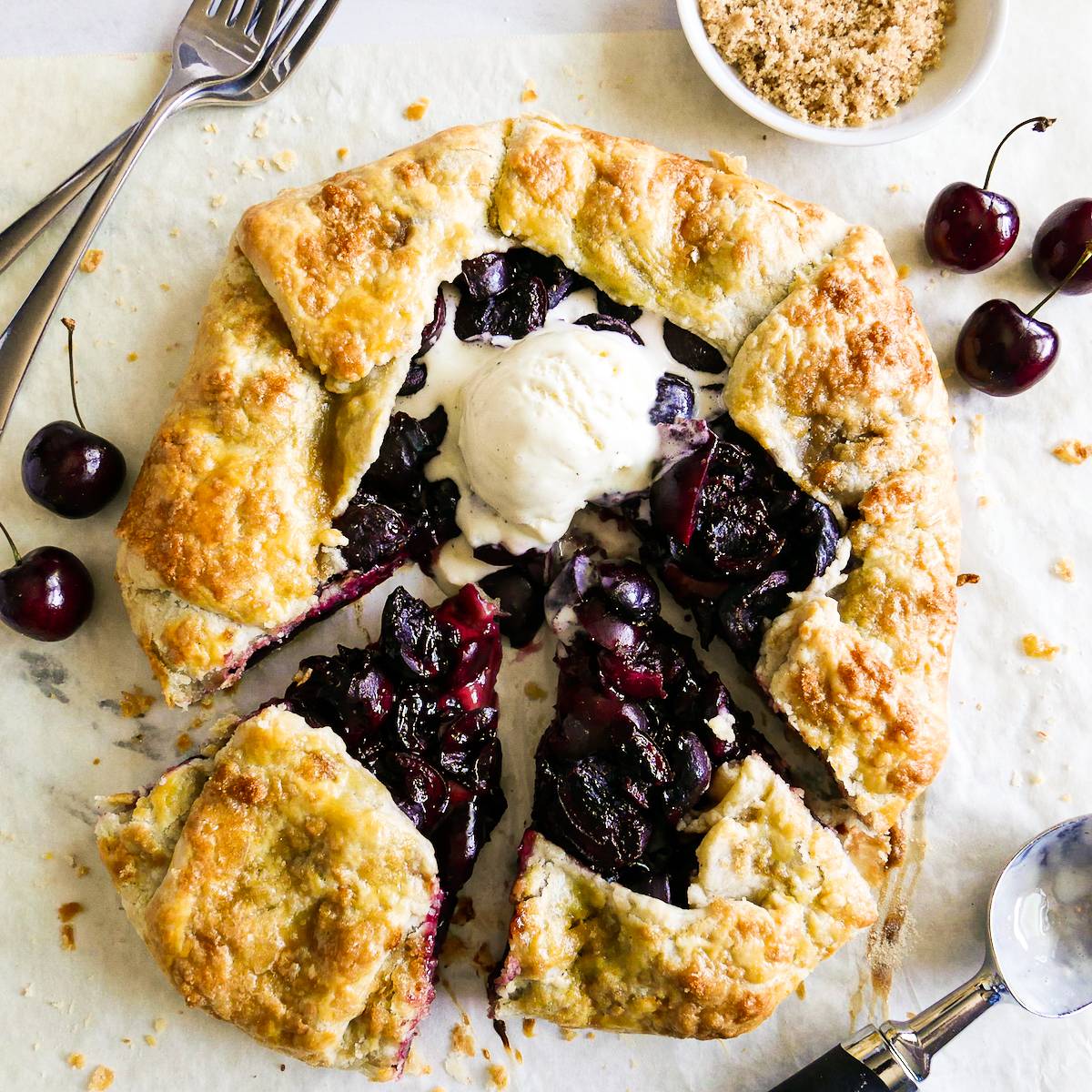 Sliced cherry galette topped with a scoop of vanilla ice cream. 