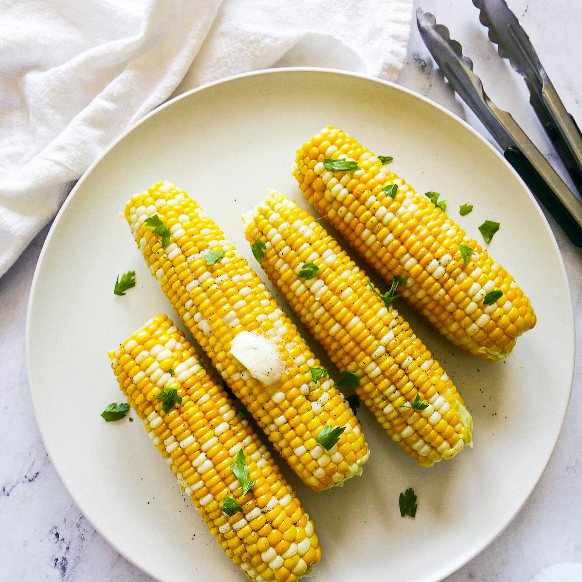 Four ears of corn on the cob on a large white platter.
