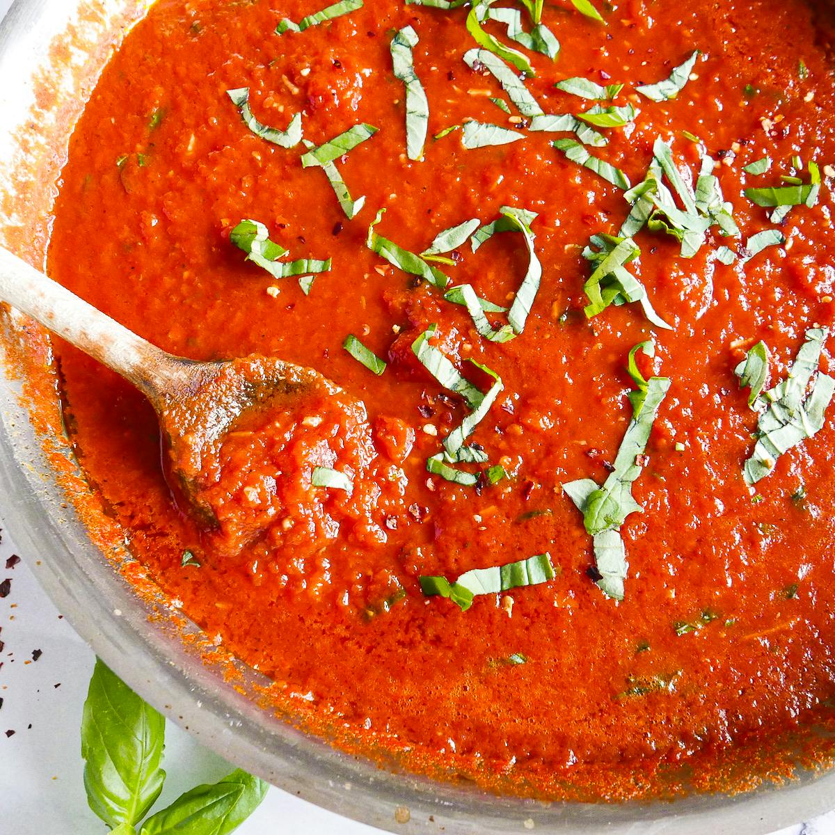 Homemade tomato sauce in a large skillet with a wooden spoon.