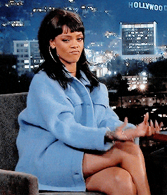 We see Rihanna in an armchair during an interview, wearing a light blue coat and large hoop earrings. Looking straight at us, she rubs her fingers and thumbs together as if to say "let's talk money."