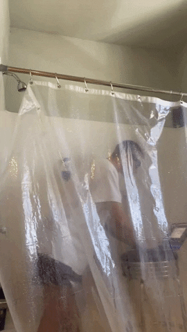 GIF of shower curtain pulled back to reveal a fully clothed college guy in the shower brushing his teeth and typing on his laptop.