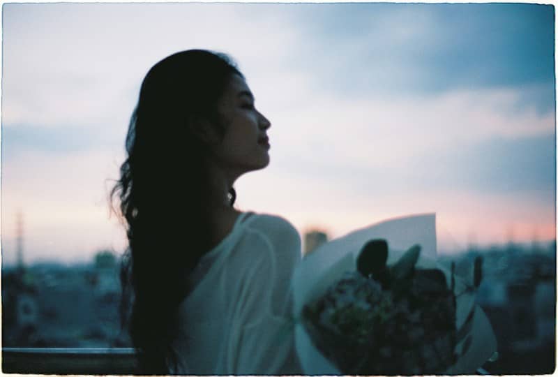 Woman holding flowers against a twilight sky