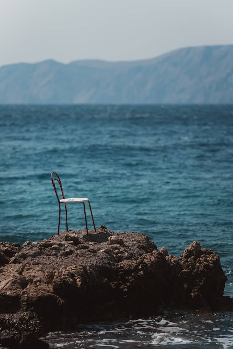 A lone chair sits on rocks by the sea.