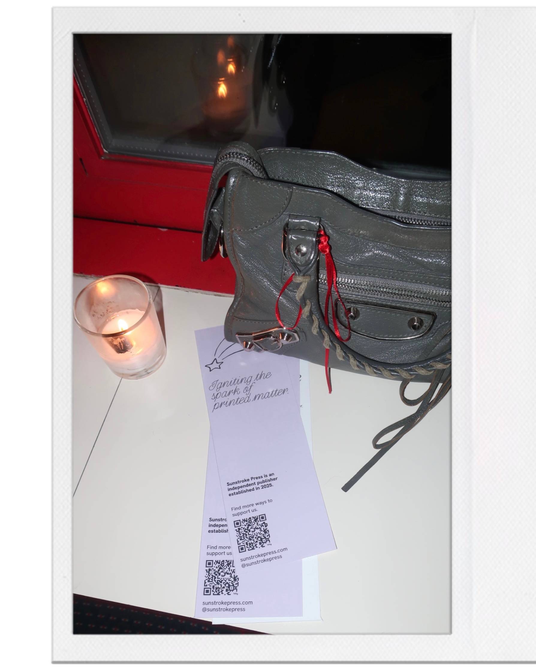 A few bookmarks lay under a handbag on a table, with a tea candle to the side.