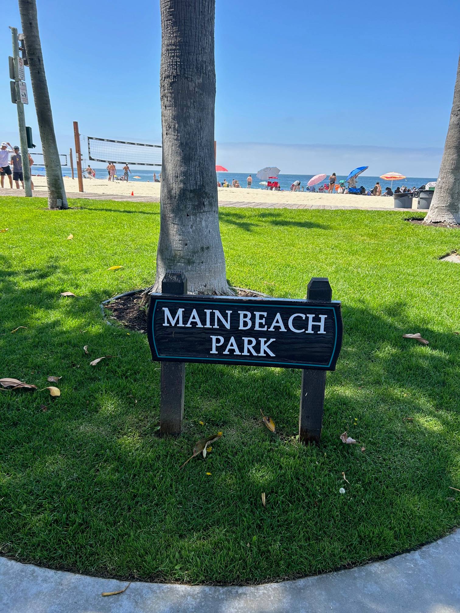 A sign "Main Beach Park" on grass, in front of a sandy beach.