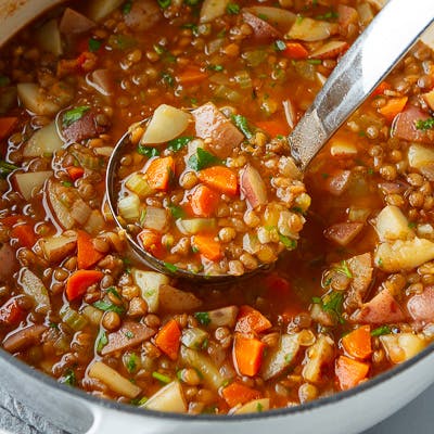 A ladle and saucepan full of lentil and potato soup.