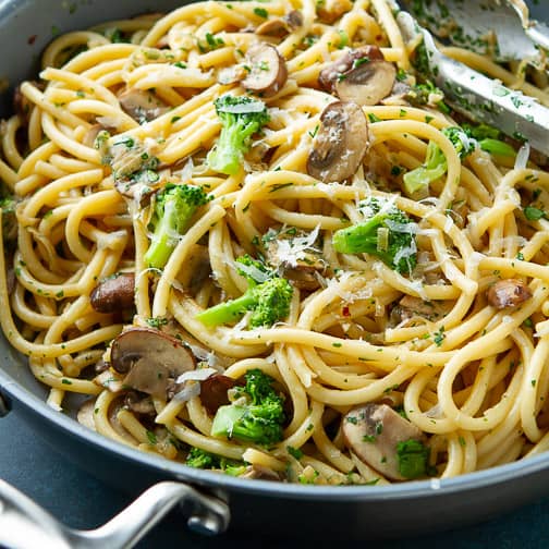 Pasta in a skillet with mushrooms and broccoli.