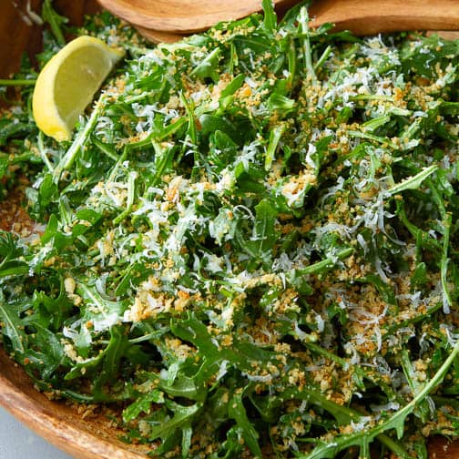 Arugula salad with breadcrumbs and grated cheese in a wooden bowl.