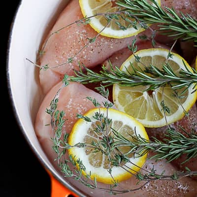 Raw chicken breasts, lemon slices and rosemary sprigs in a large saucepan.