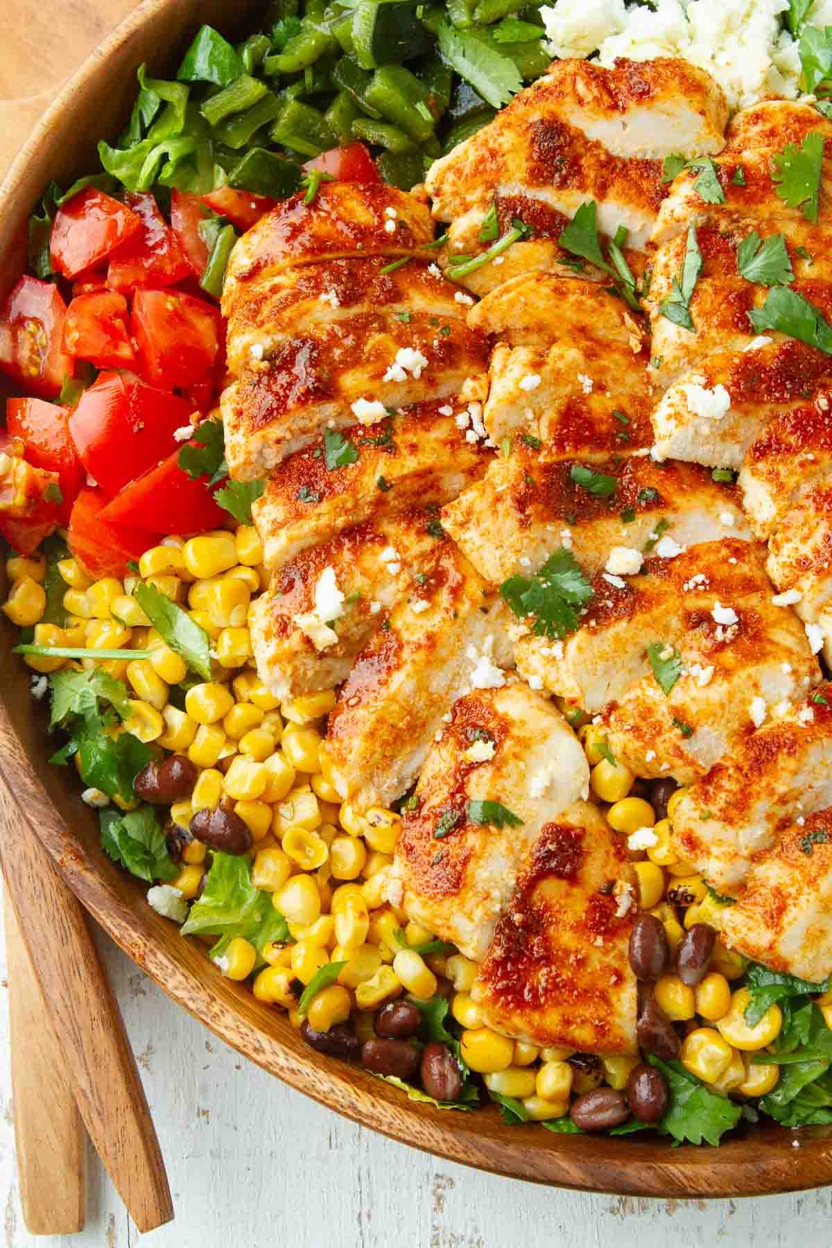 Spiced chicken, lettuce, tomato, corns and beans in a wooden bowl.
