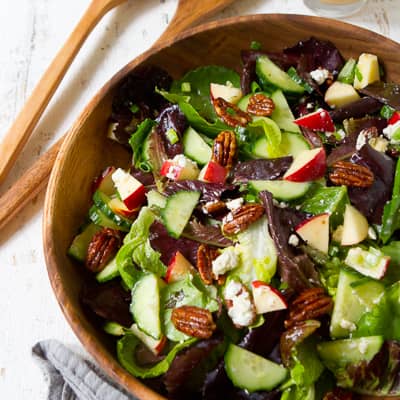 A salad with nuts and apple in a wooden bowl.