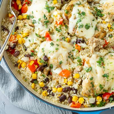 A large skillet filled with cheese-topped chicken, quinoa and vegetables.