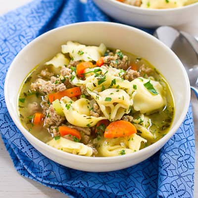 Tortellini and turkey soup in a white bowl.
