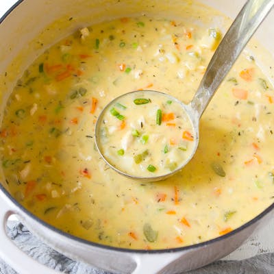 A ladle scooping creamy chicken soup out of a saucepan.