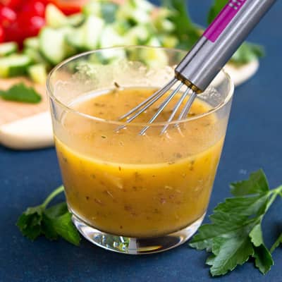 Greek dressing in a small glass with a whisk.