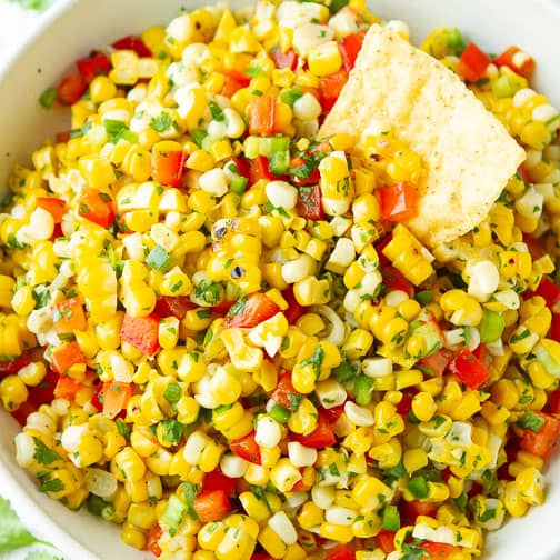 Fresh corn salsa and a tortilla chip in a white bowl.