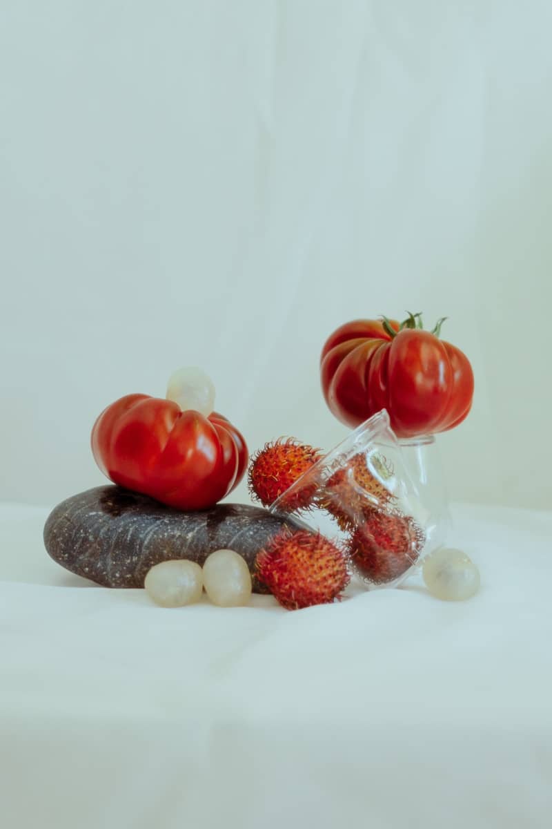 Tomatoes, rambutan, and grapes on stones.