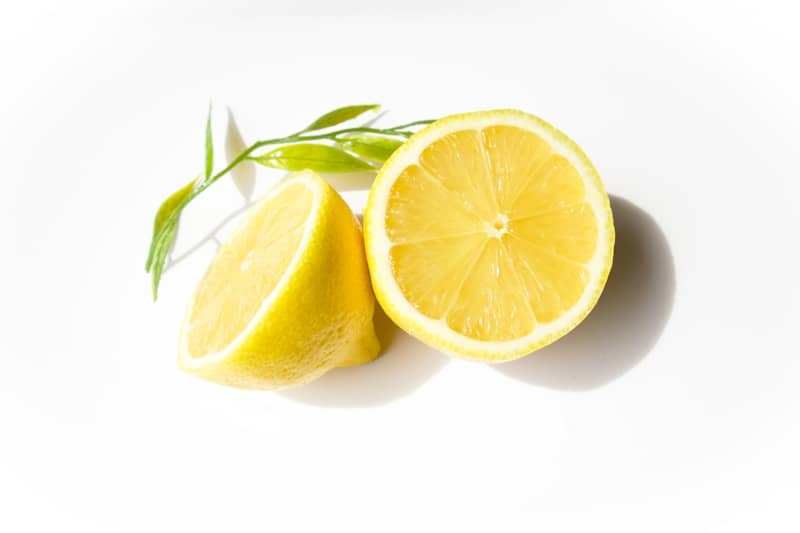A sliced lemon with green leaves on white.