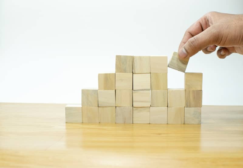 A person placing a block into a pile of wooden blocks