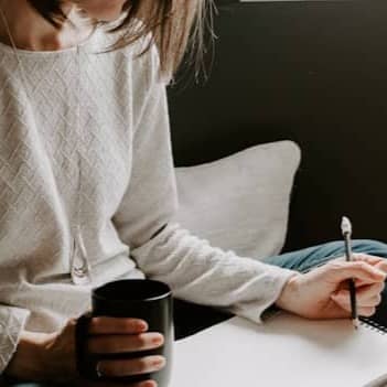 Woman writing in notebook with coffee cup