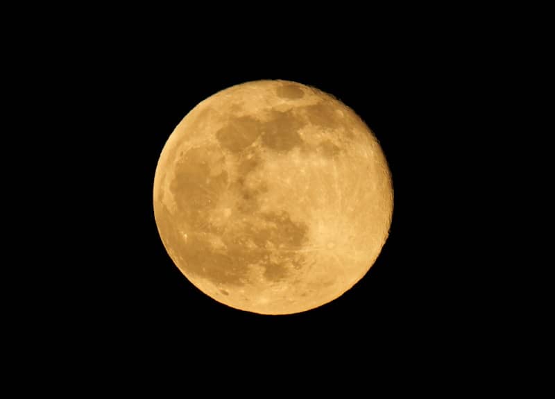 A full moon is seen in the dark sky