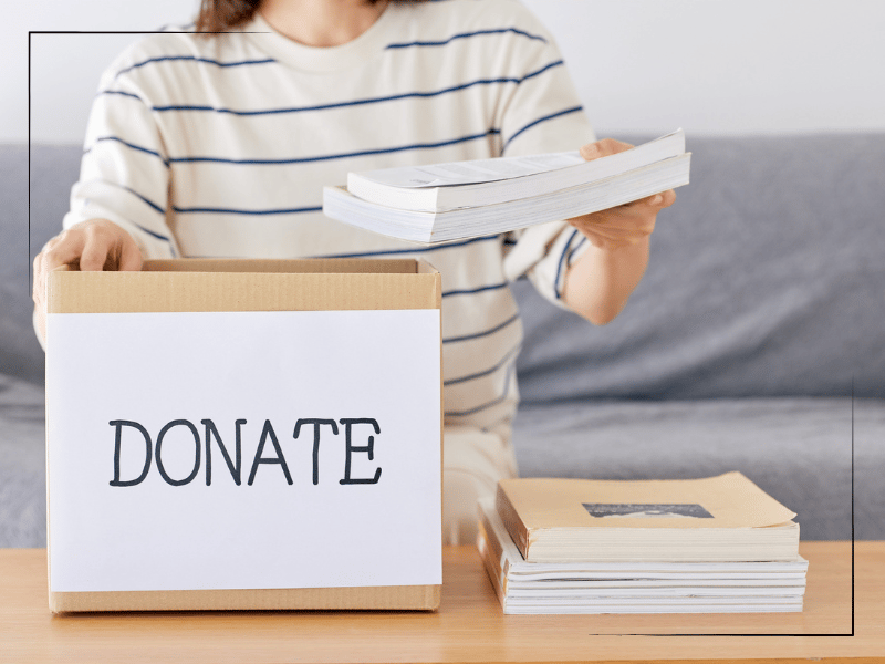 Woman decluttering books into box labeled "DONATE"