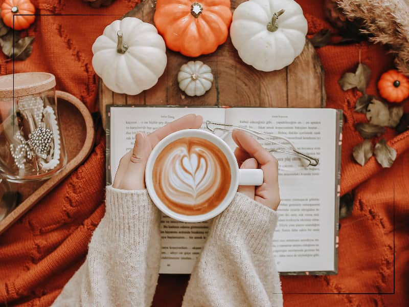 Woman holding coffee mug over book and Fall-themed table