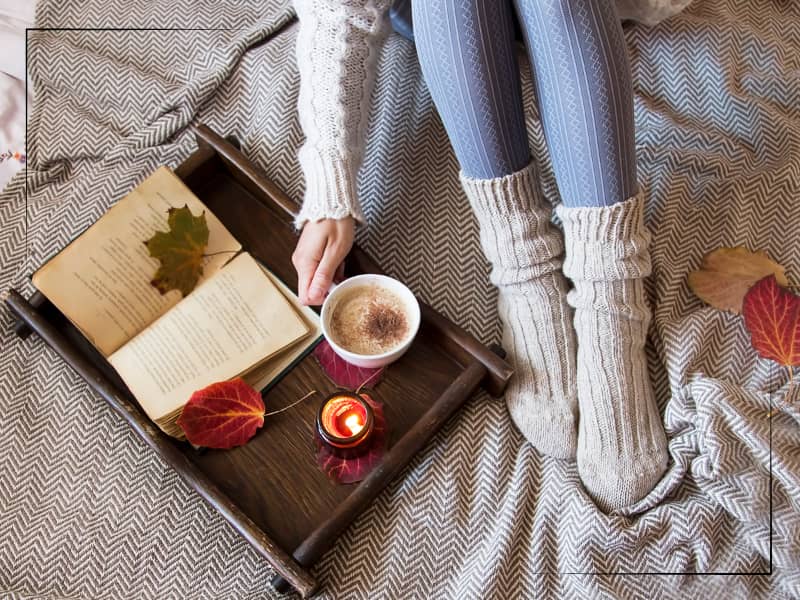 book and mug on bed with woman holding mug