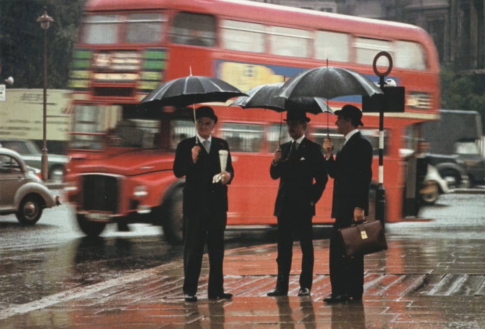 Three men stand in the rain holding umbrellas
