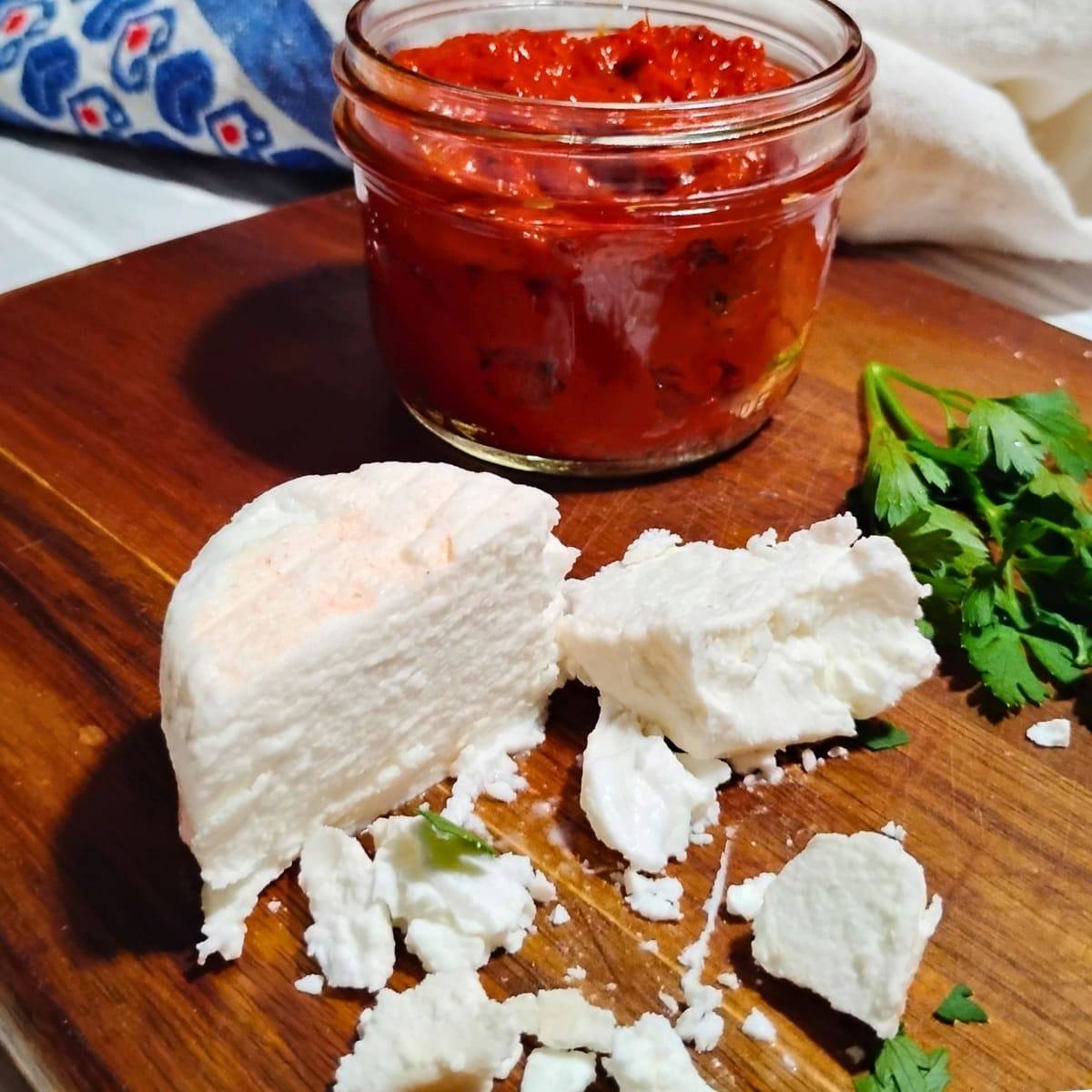 soft feta cheese on a cutting board with some ajvar in a jar behind it.