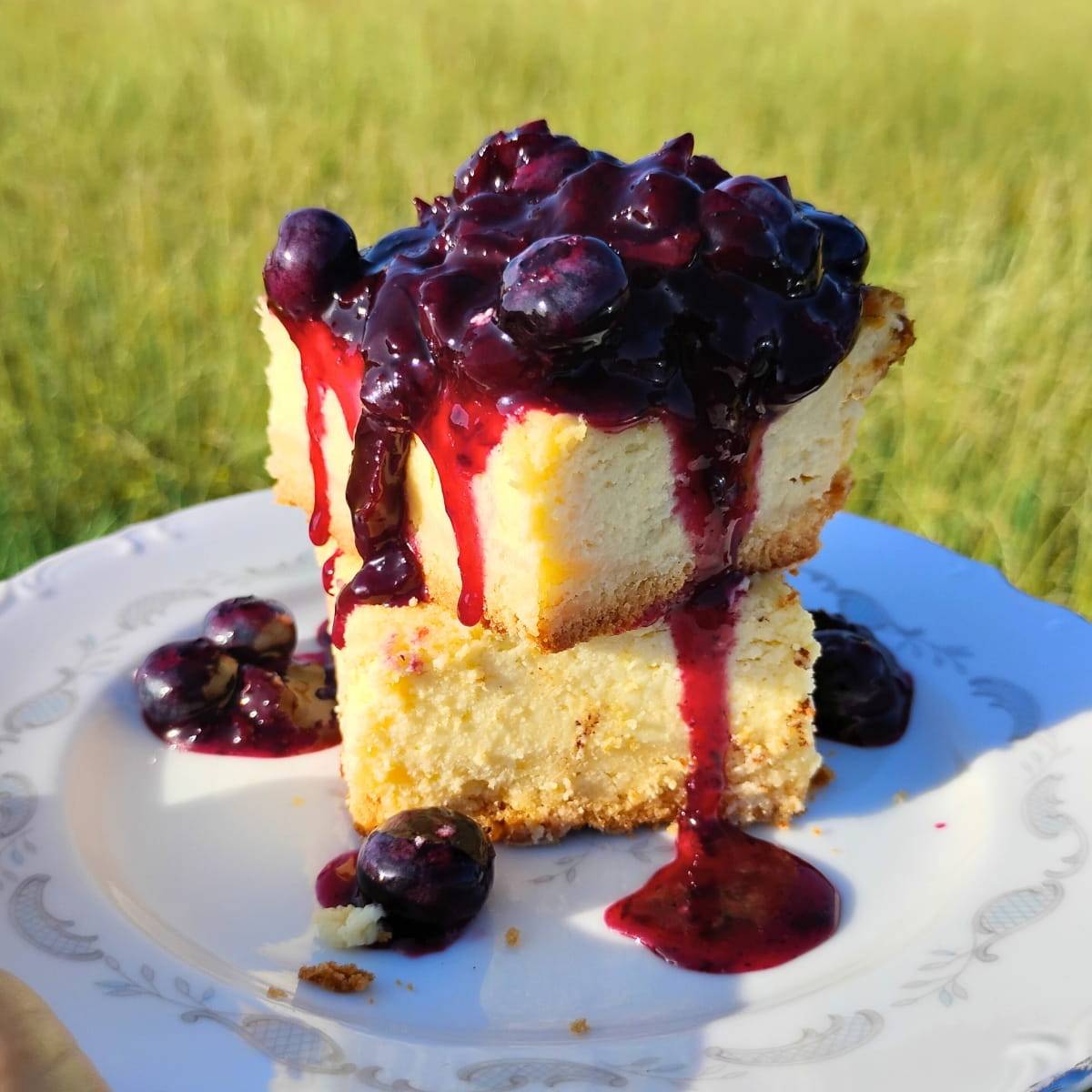 photo of a couple of cheese cake pieces stacked on top of each other with blueberry sauce running down on it.