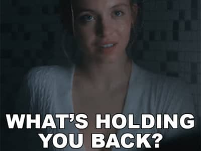 Sydney Sweeney wearing a white or light-colored top, photographed in dim lighting with a serious or contemplative expression. Text overlay at the bottom reads 'WHAT'S HOLDING YOU BACK?' in bold white capital letters.