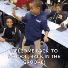 A person in a blue jacket enthusiastically raises their arms in celebration while seated at what appears to be a desk or table with papers. Text overlay reads 'WELCOME BACK TO SCHOOL! BACK IN THE GROOVE!' The person appears excited and energetic, embodyin