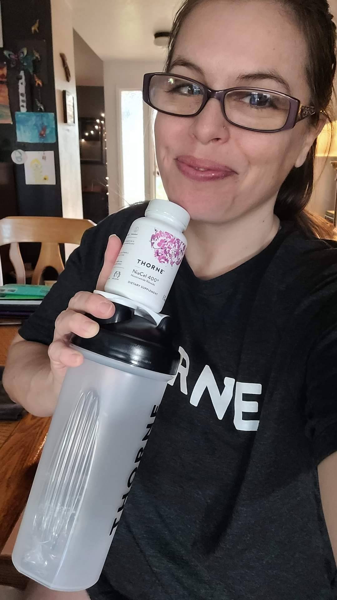 woman sits smiling with her supplements and protein shaker