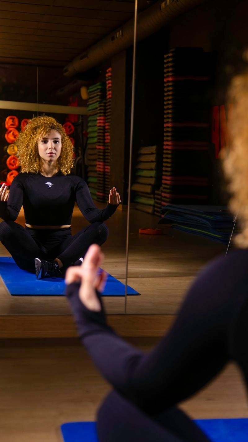 A woman meditates on a mat in front of a mirror.