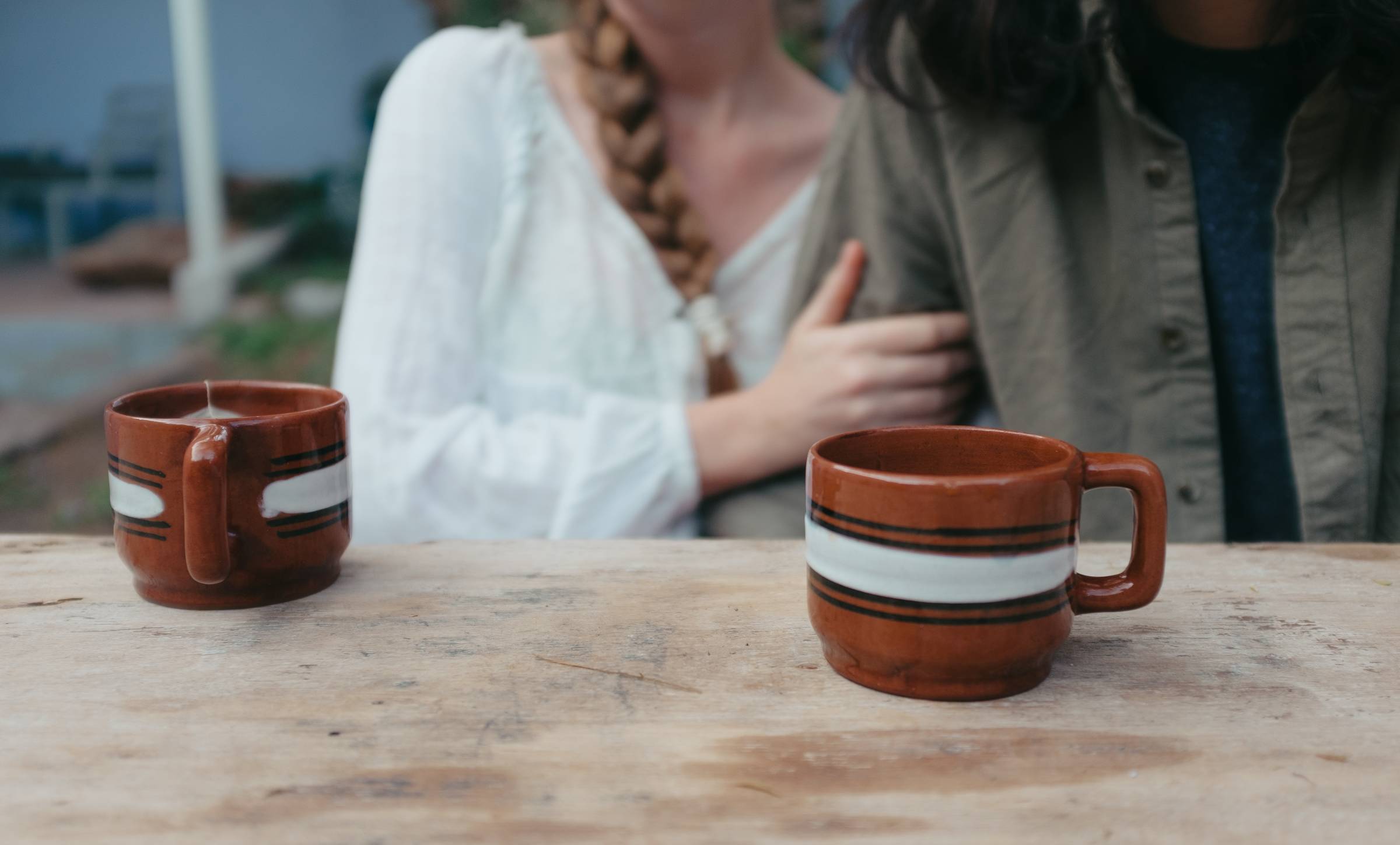 two coffee cups sit on the table in the foreground while a couple can be seen behind them in the background