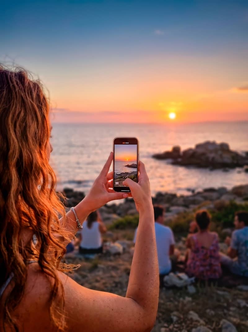 Woman photographs stunning ocean sunset with her smartphone.