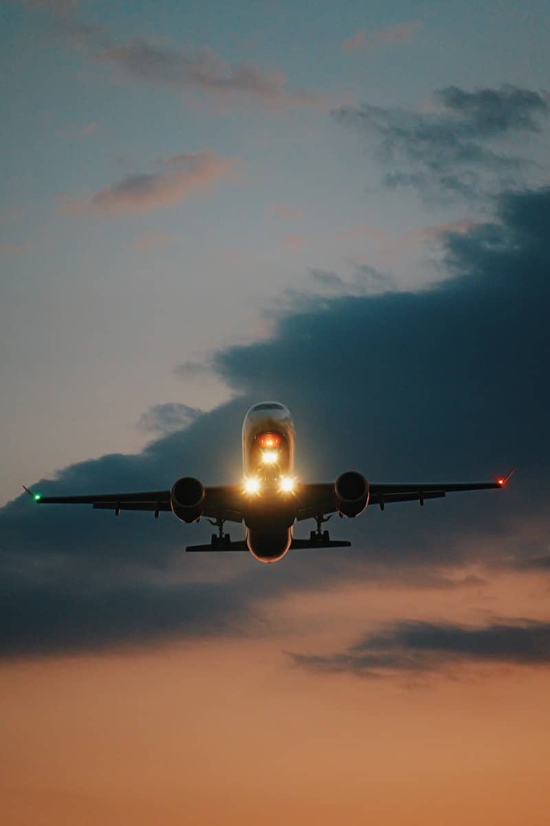 Airplane with bright landing lights against a twilight sky.