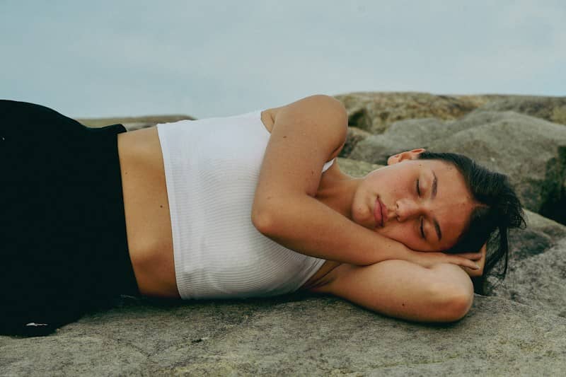 A woman in a white crop top resting on grey rocks