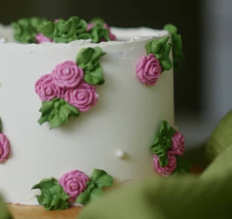 A white cake decorated with pink frosting roses and green leaves
